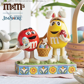 Jim Shore M&M'S Easter figurine of Red and Yellow with decorated eggs beside an Easter basket